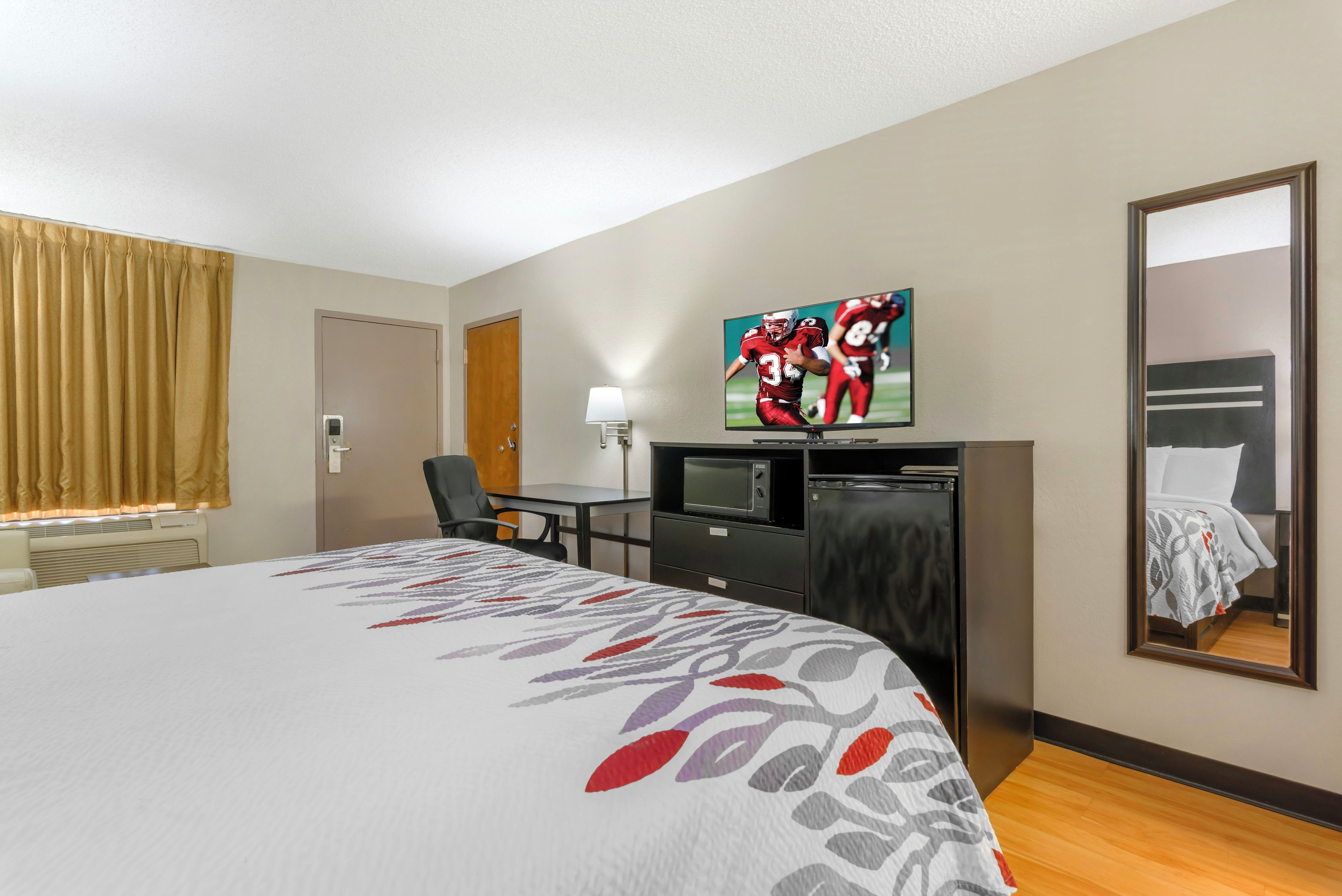 A hotel room with a large bed, a desk with a computer, a television, and a mirror.