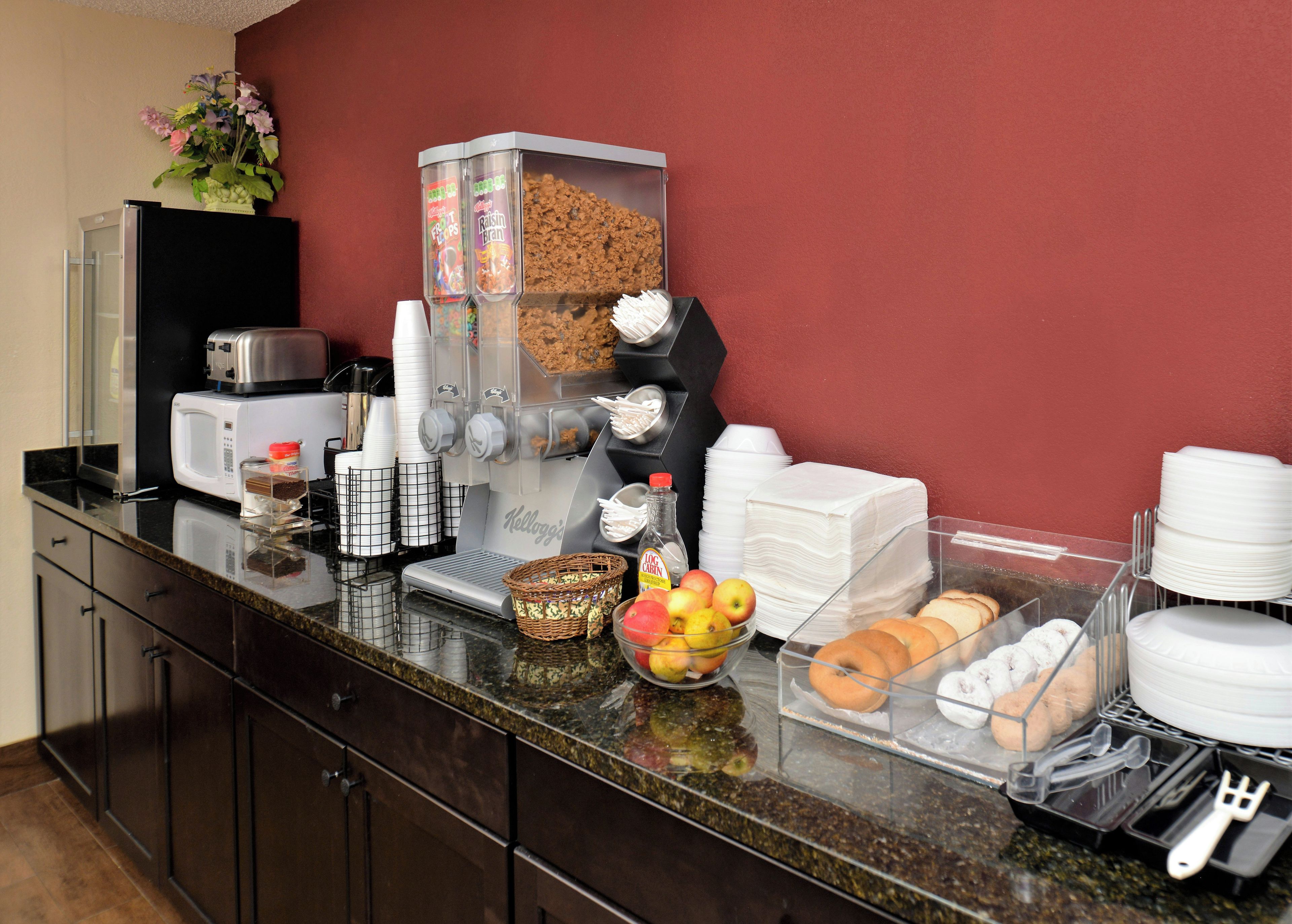 Montaje de un bufé de desayuno con una máquina de café, dispensadores de cereales y diversas opciones de comida.
