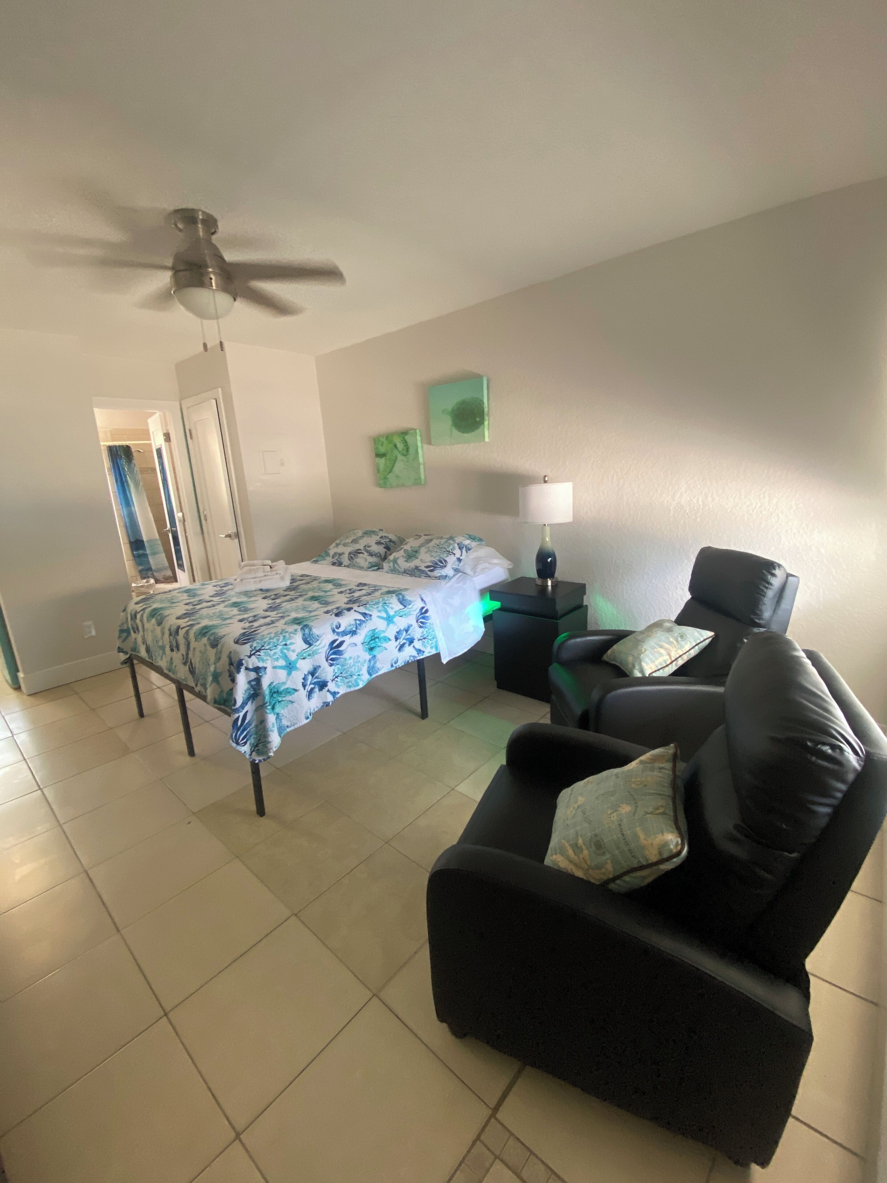 A bedroom with a bed, a chair, a nightstand, a lamp, and a ceiling fan.