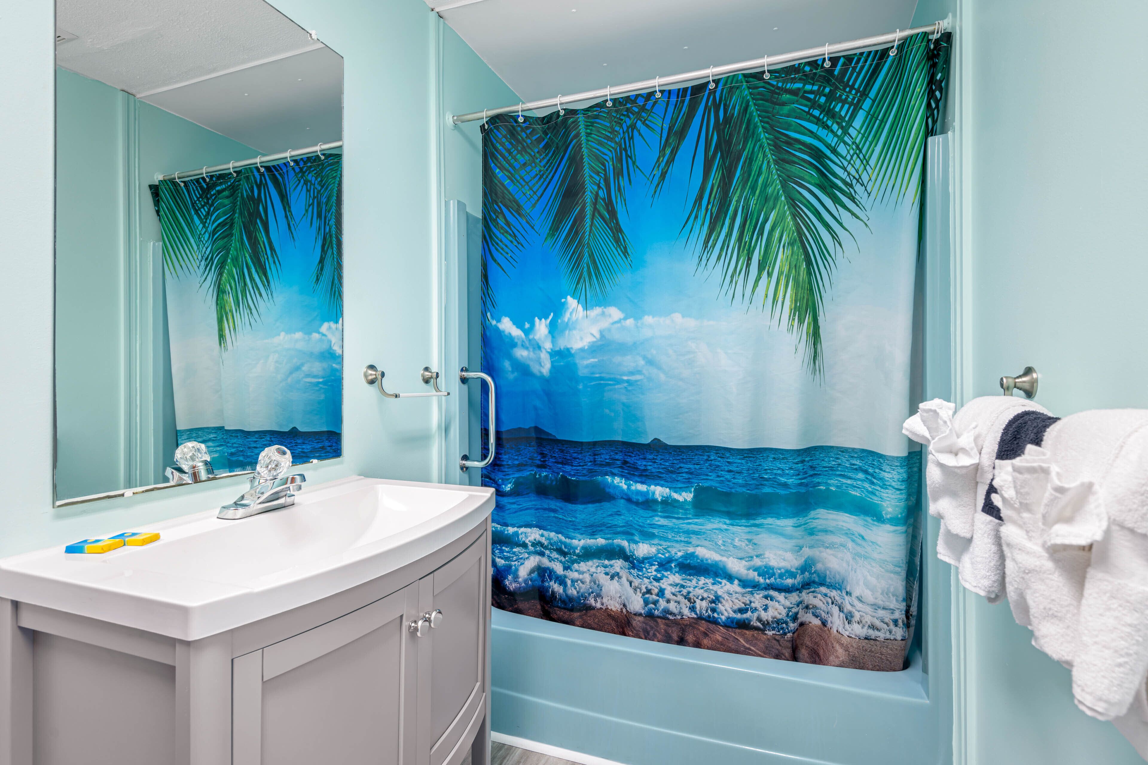 Un baño con un espejo grande, un lavabo y una cortina de ducha con un paisaje playero.