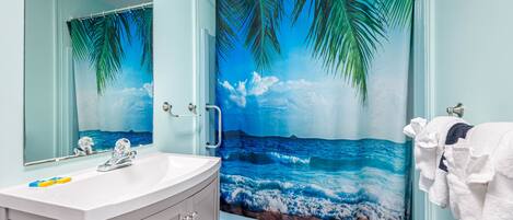 Un baño con un espejo grande, un lavabo y una cortina de ducha con un paisaje playero.