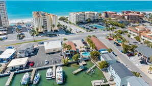 A coastal marina with several boats docked, a parking lot, and buildings with balconies overlooking the beach. - Sand Vista Vacation Rentals (Redington Shores)