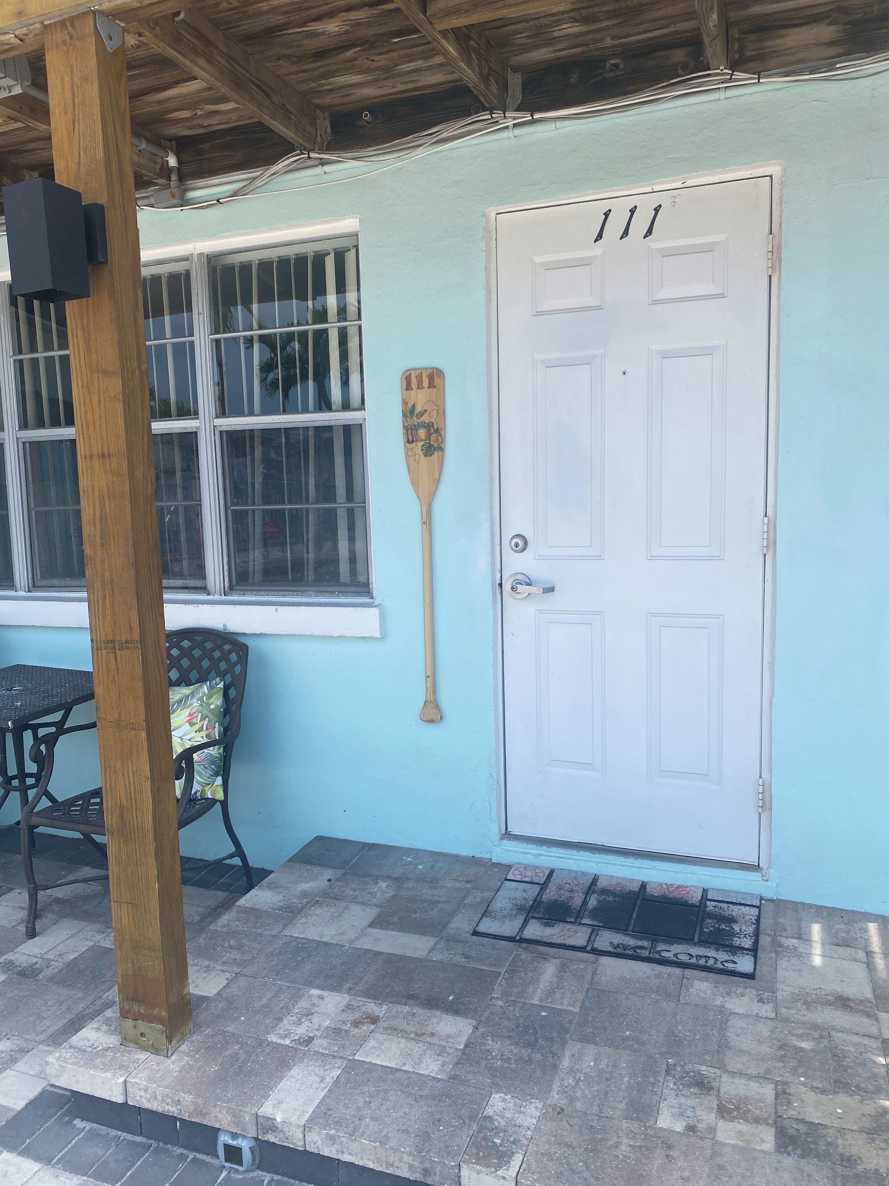 A door with the number 111, a wooden paddle leaning against the wall, and a 'welcome' mat at the entrance.