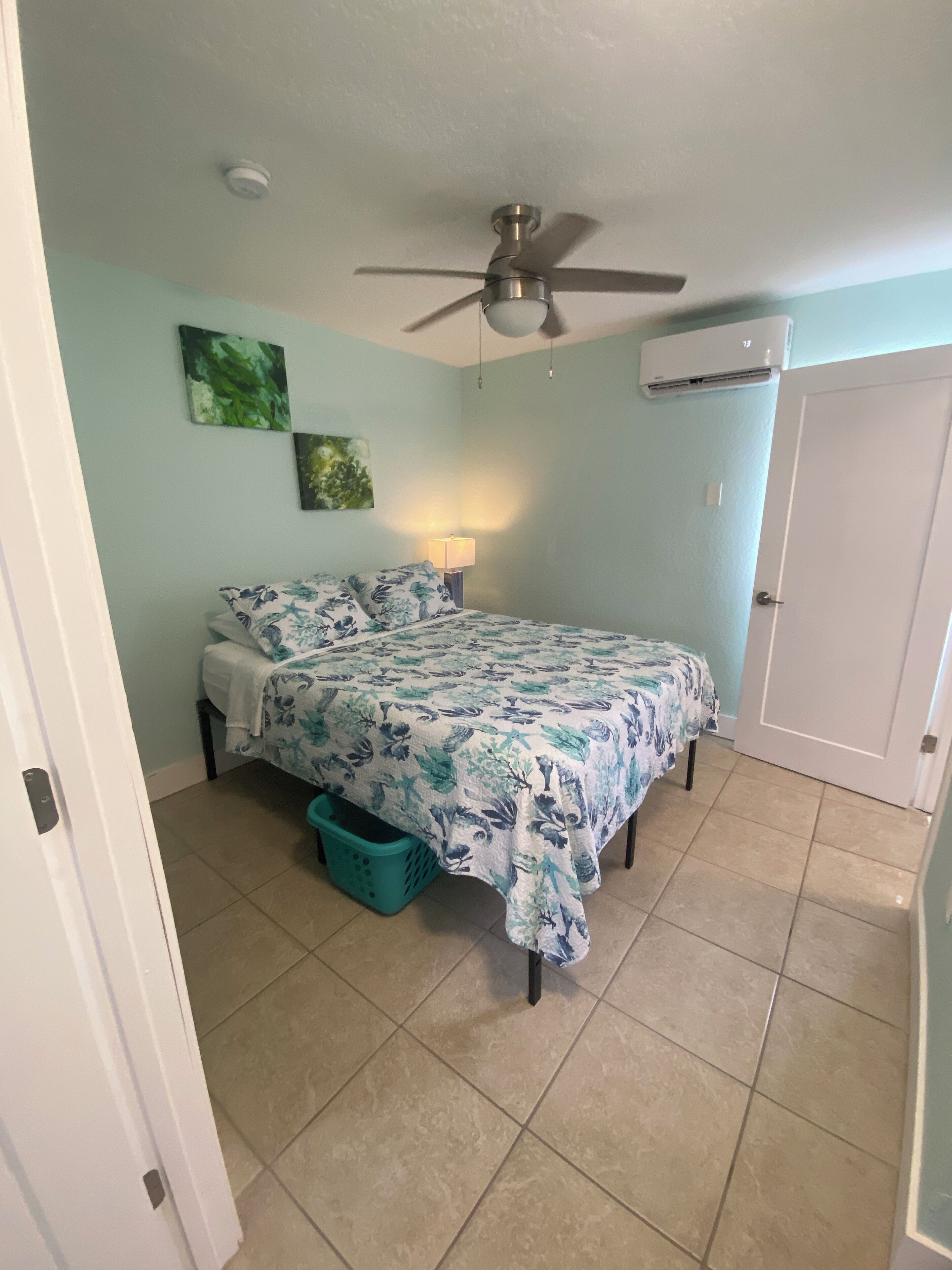 A bedroom with a bed, a ceiling fan, an air conditioning unit, and a door.