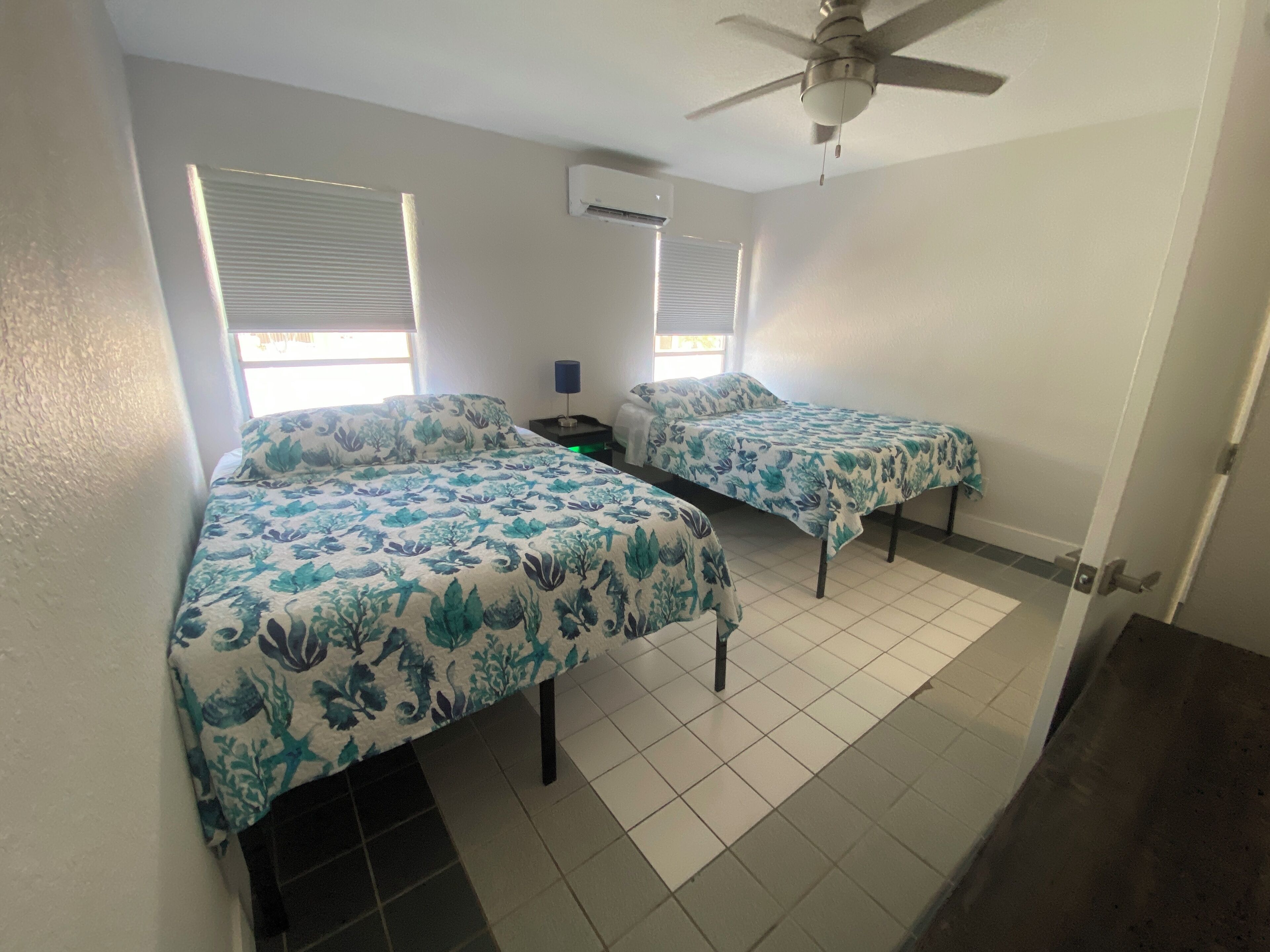 A bedroom with two beds, a ceiling fan, and an air conditioning unit.