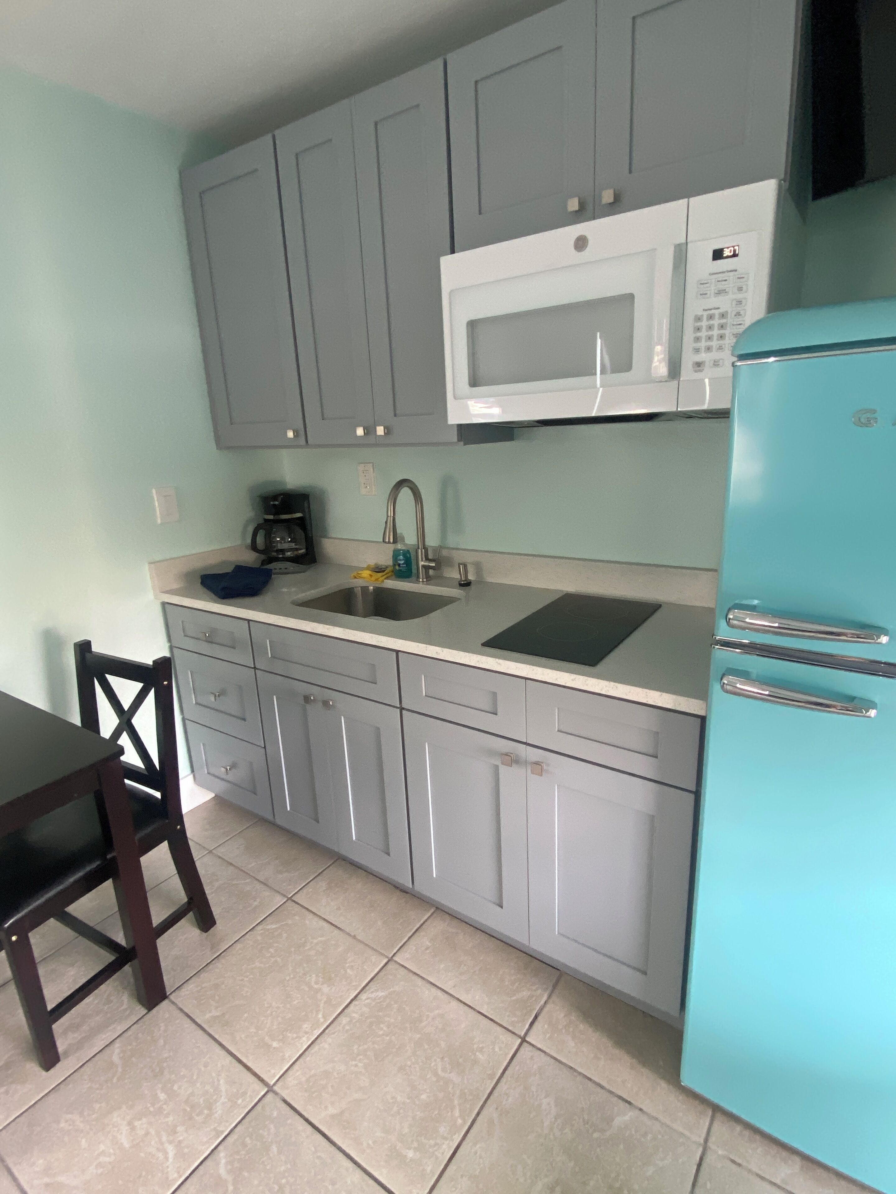 Une cuisine avec des meubles de couleur grise, un micro-ondes blanc, un évier et un réfrigérateur de couleur turquoise.