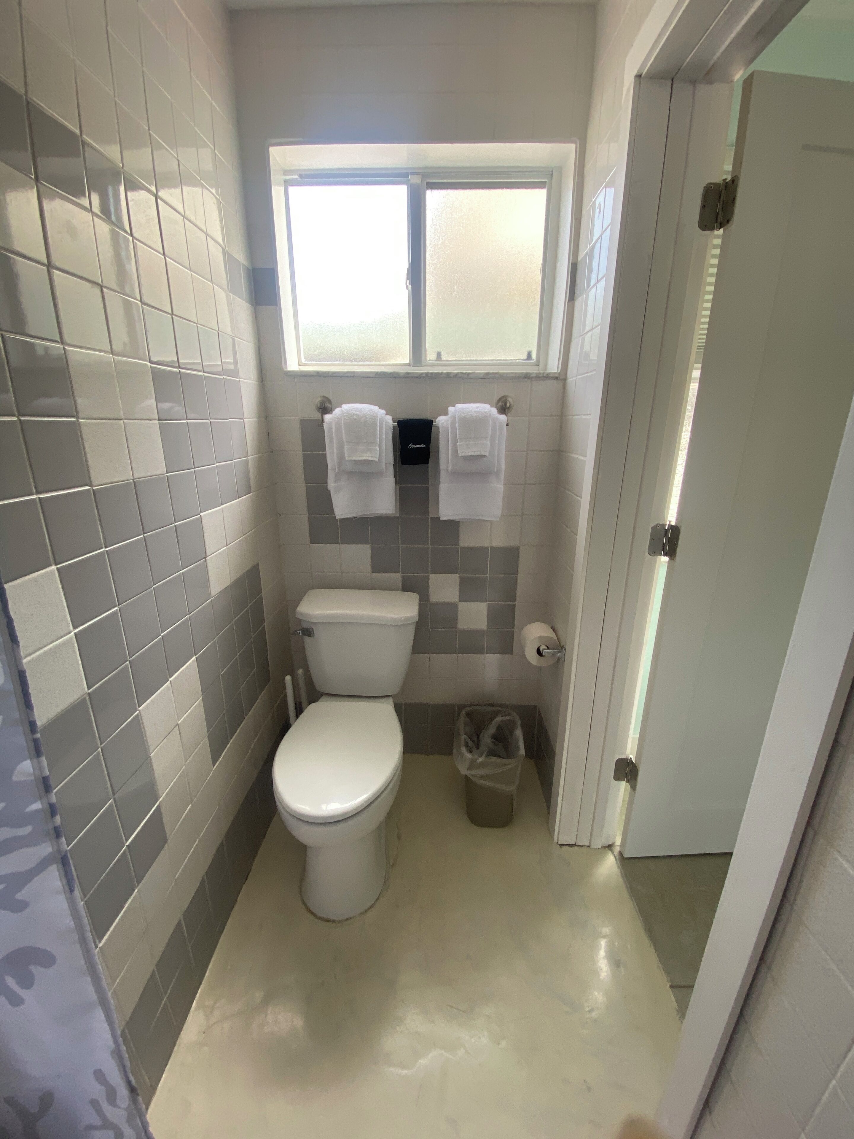 A small bathroom with a toilet, a window, and two towels hanging on hooks.