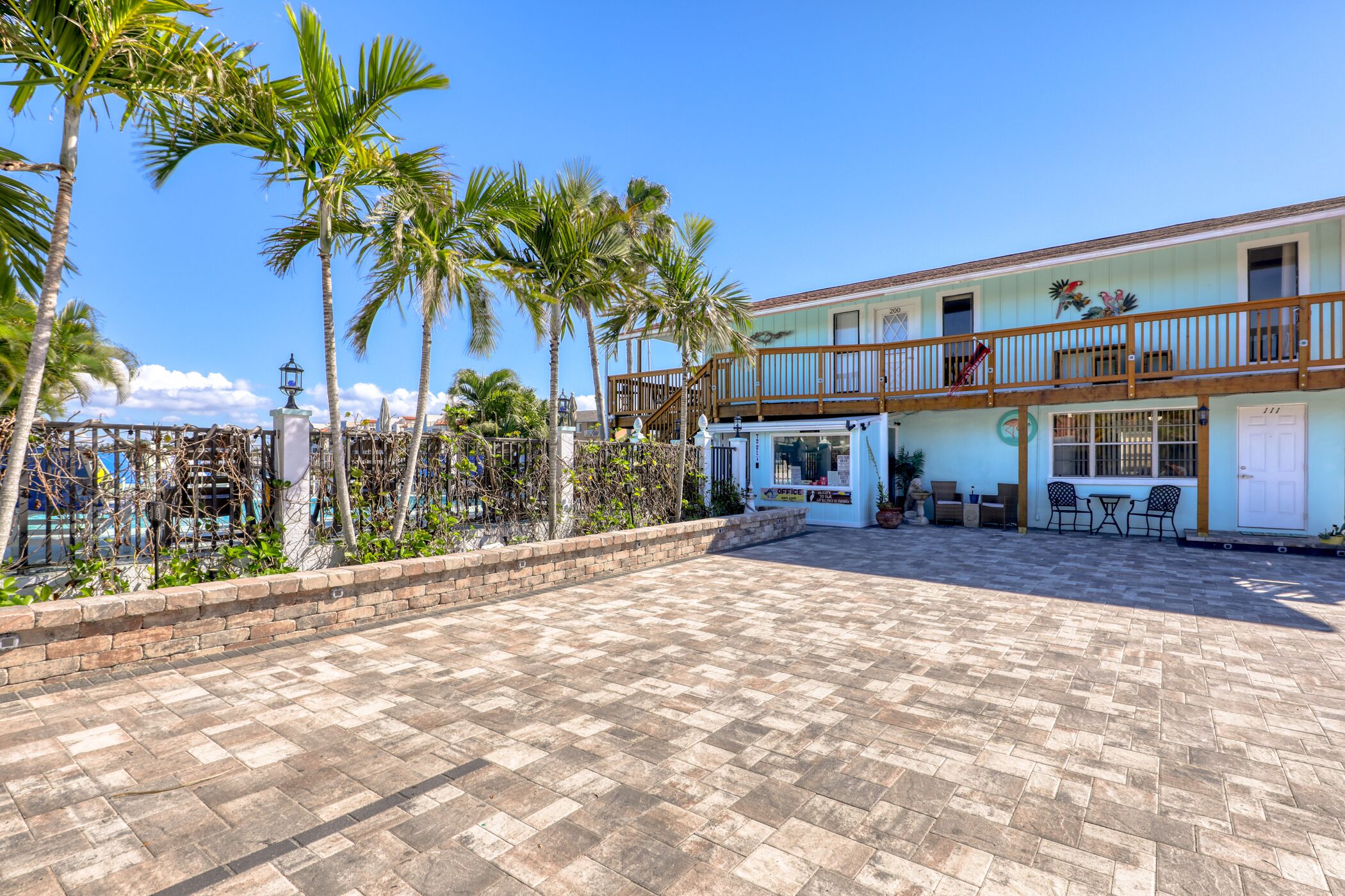 A two-story building with a balcony, outdoor seating area, and palm trees.