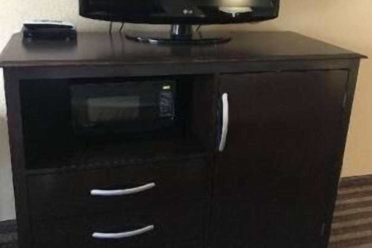 A black TV stand with a flat-screen TV, a small speaker, and three drawers.