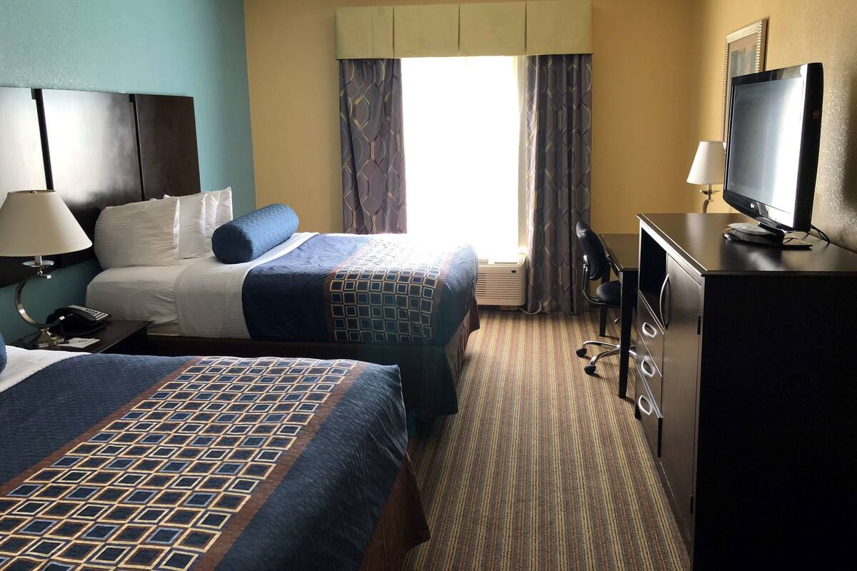 A hotel room with two beds, a desk with a computer, a television, and a window with curtains.