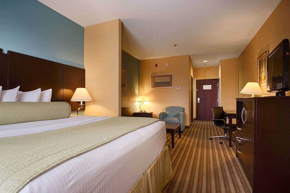 A hotel room with a large bed, a desk, a chair, a television, and a door.
