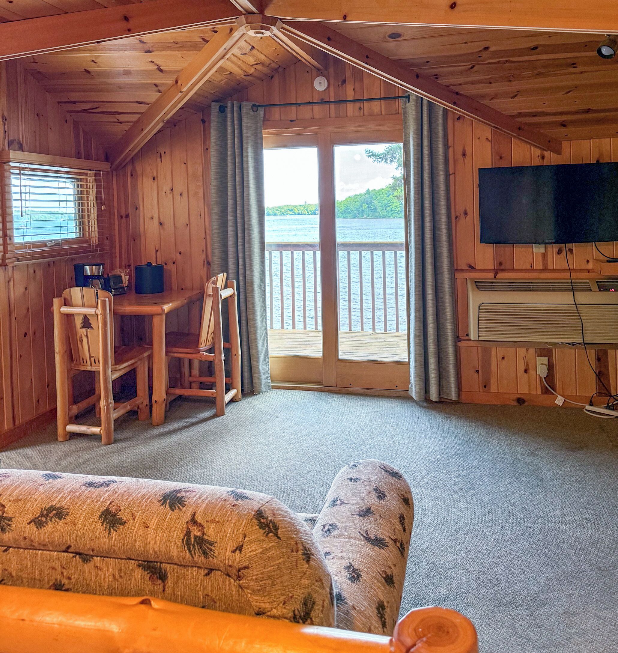 A cabin with a dining area, a television, and a view of a lake.