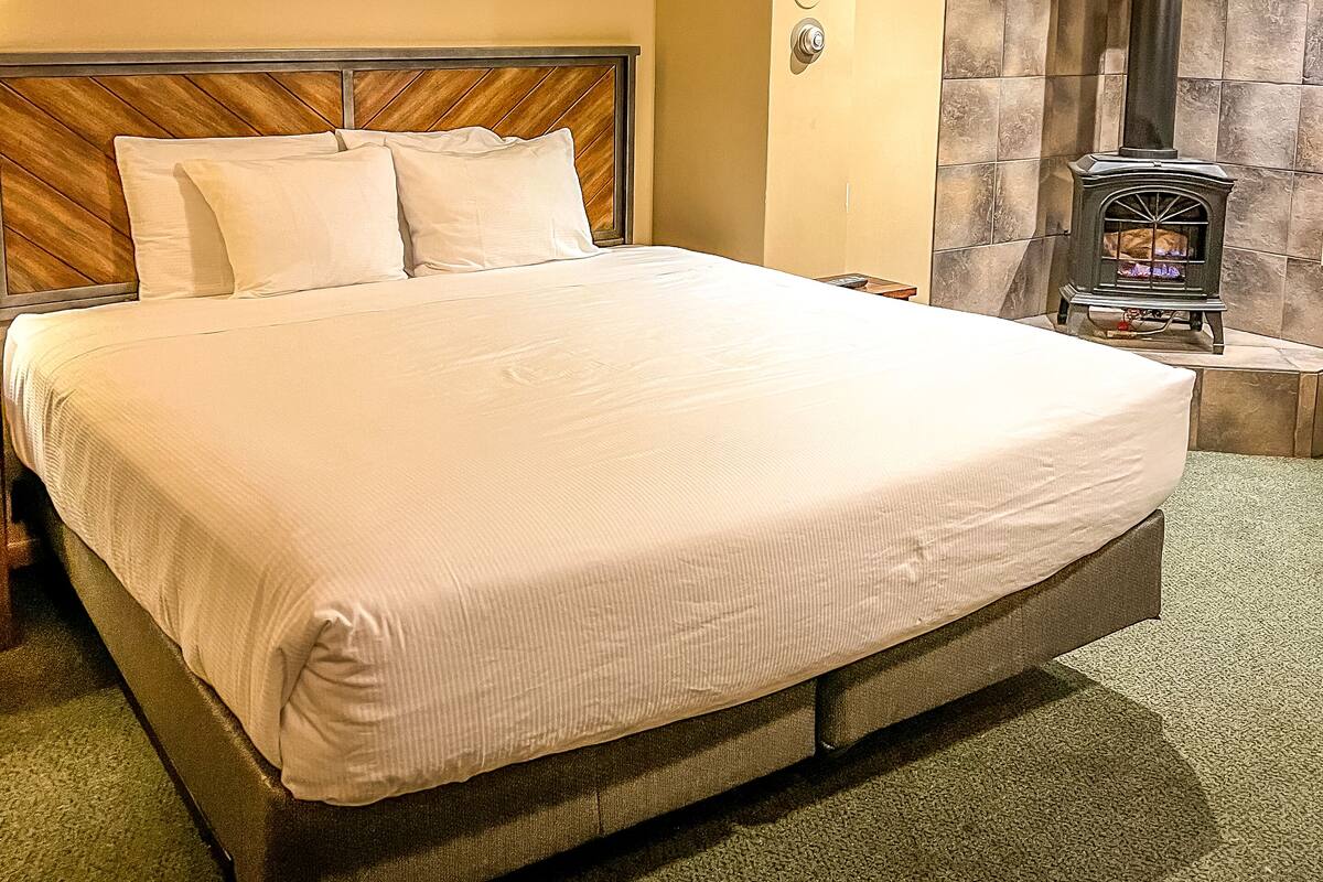 Una cama grande con sábanas blancas en una habitación con paredes color beige y chimenea de piedra.