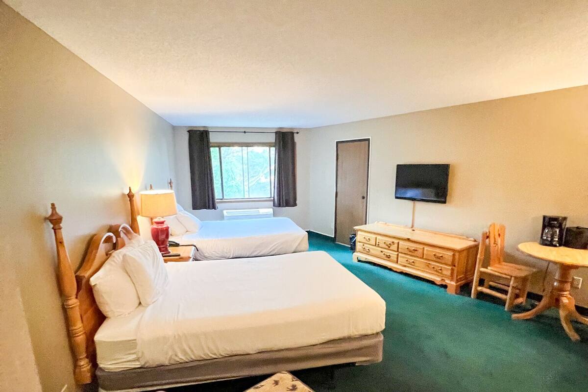 Una habitación de hotel con una cama grande, un escritorio, una silla, un televisor y una ventana con cortinas.