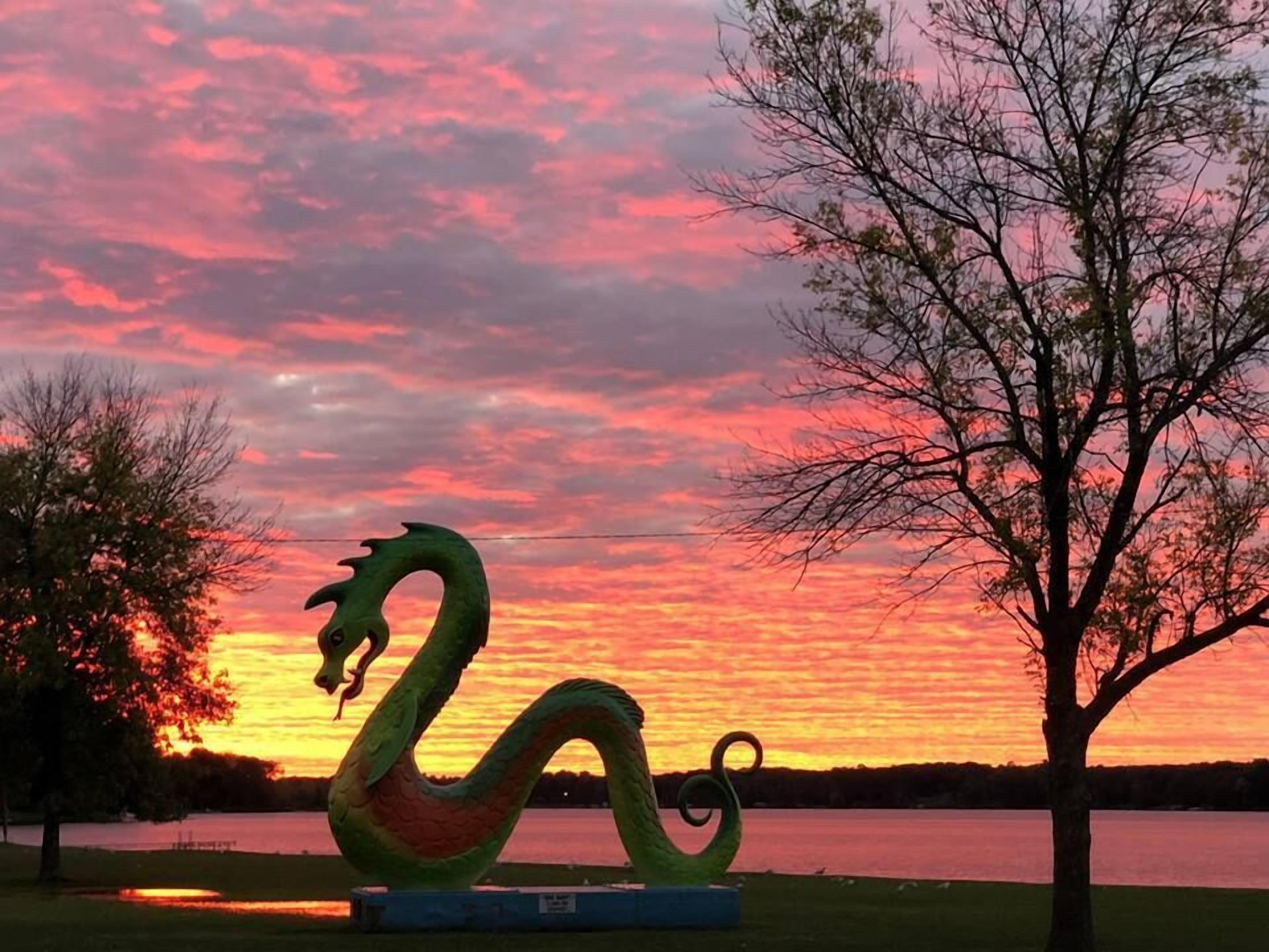 Una escultura de dragón en un parque con un atardecer de fondo.