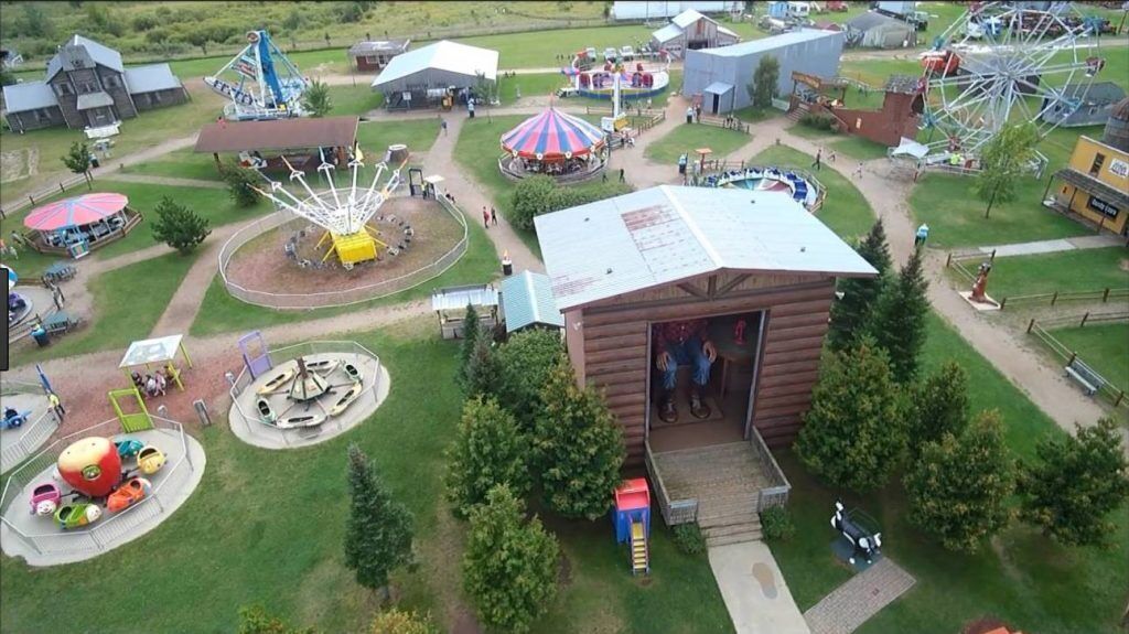 Luchtbeeld van een park met diverse attracties en gebouwen, waaronder een reuzenrad, een carrousel en een gebouw met een geopende deur.