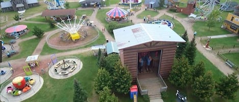 Luchtbeeld van een park met diverse attracties en gebouwen, waaronder een reuzenrad, een carrousel en een gebouw met een geopende deur.