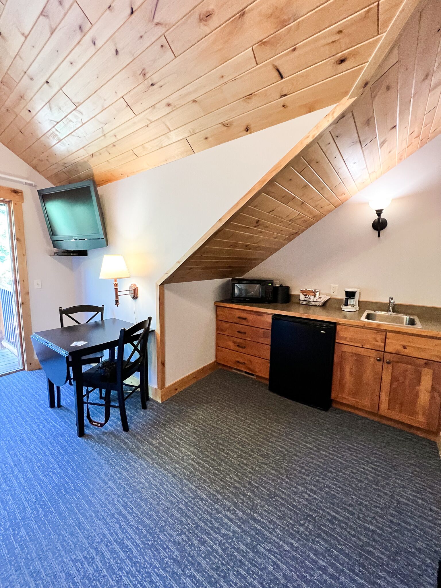 A compact kitchen with wooden cabinets, a built-in microwave, and a sink. There's a dining table with chairs and a lamp.