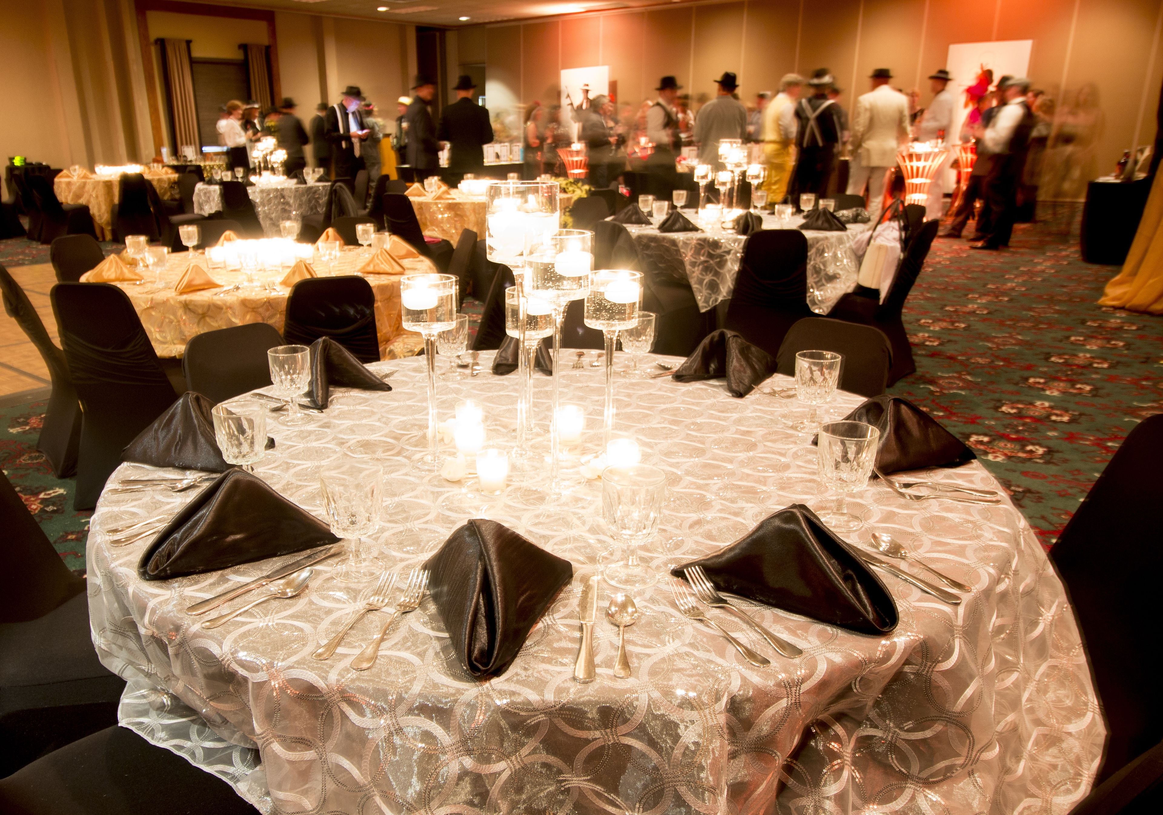 A round table set for a formal event with multiple chairs, each with a black napkin and silverware.