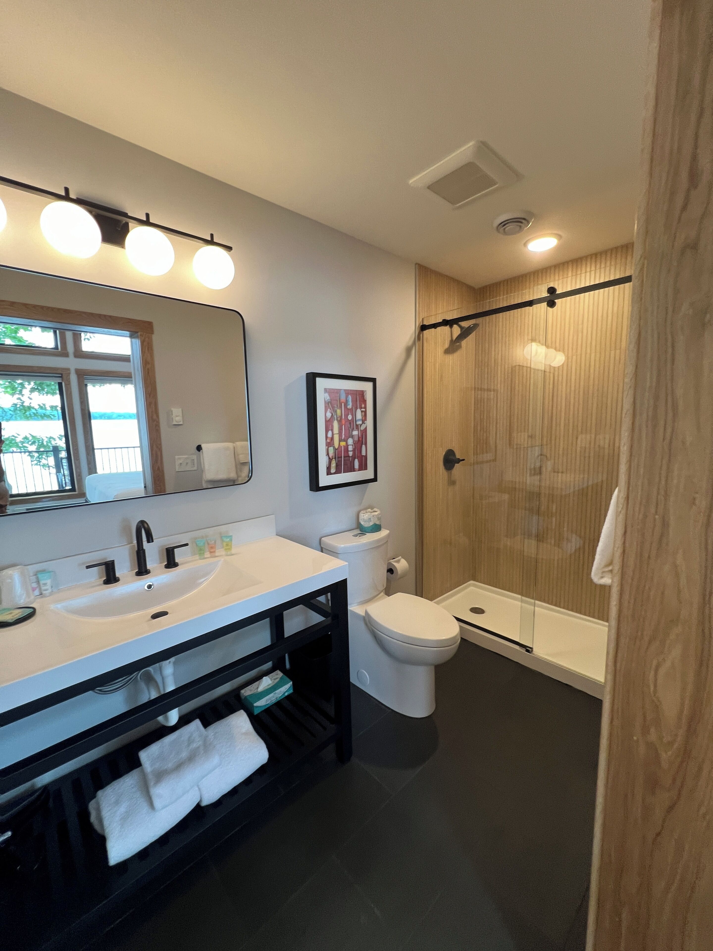 A modern bathroom with a large mirror, dual sinks, a toilet, and a glass-enclosed shower.