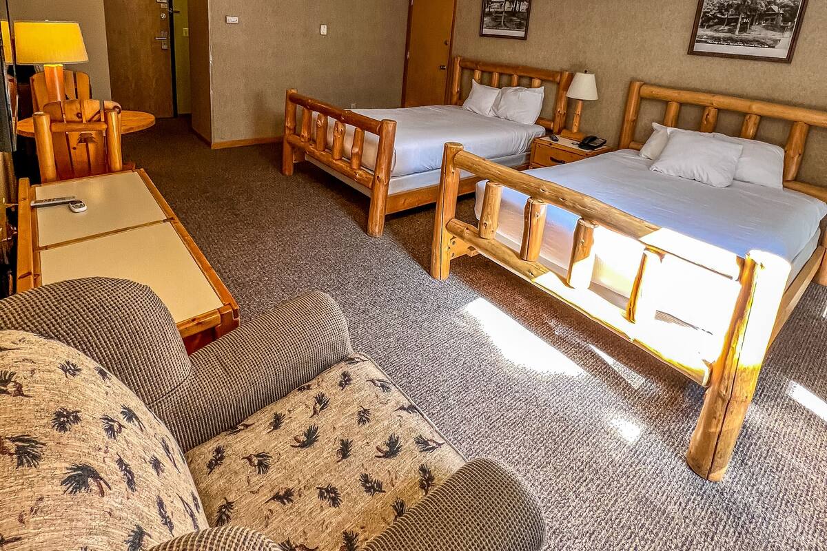 Habitación de hotel con dos camas de madera, un sofá, una mesita y una lámpara.