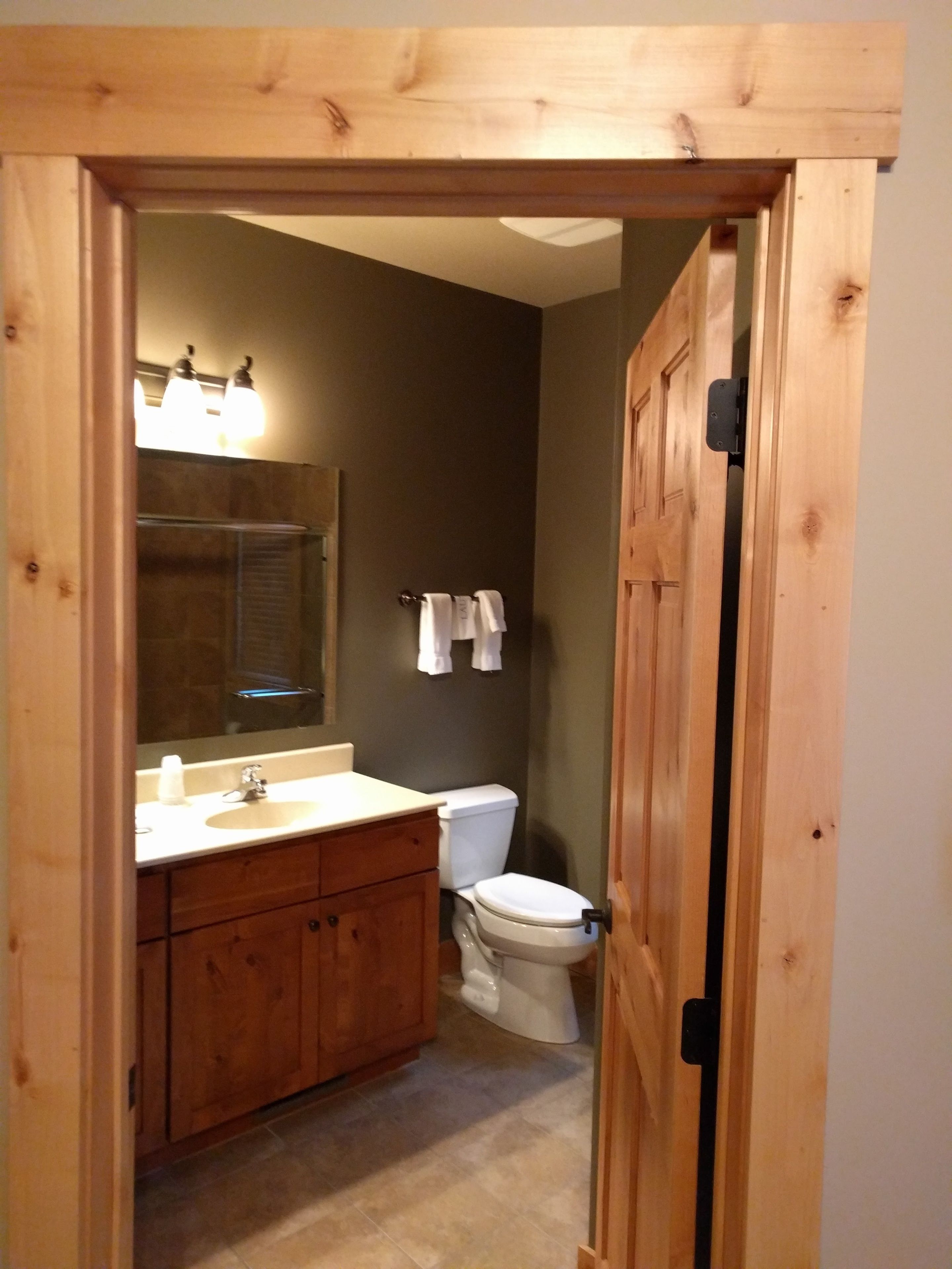 Une salle de bain avec des meubles en bois, un lavabo, des toilettes et un miroir avec des lumières au-dessus.