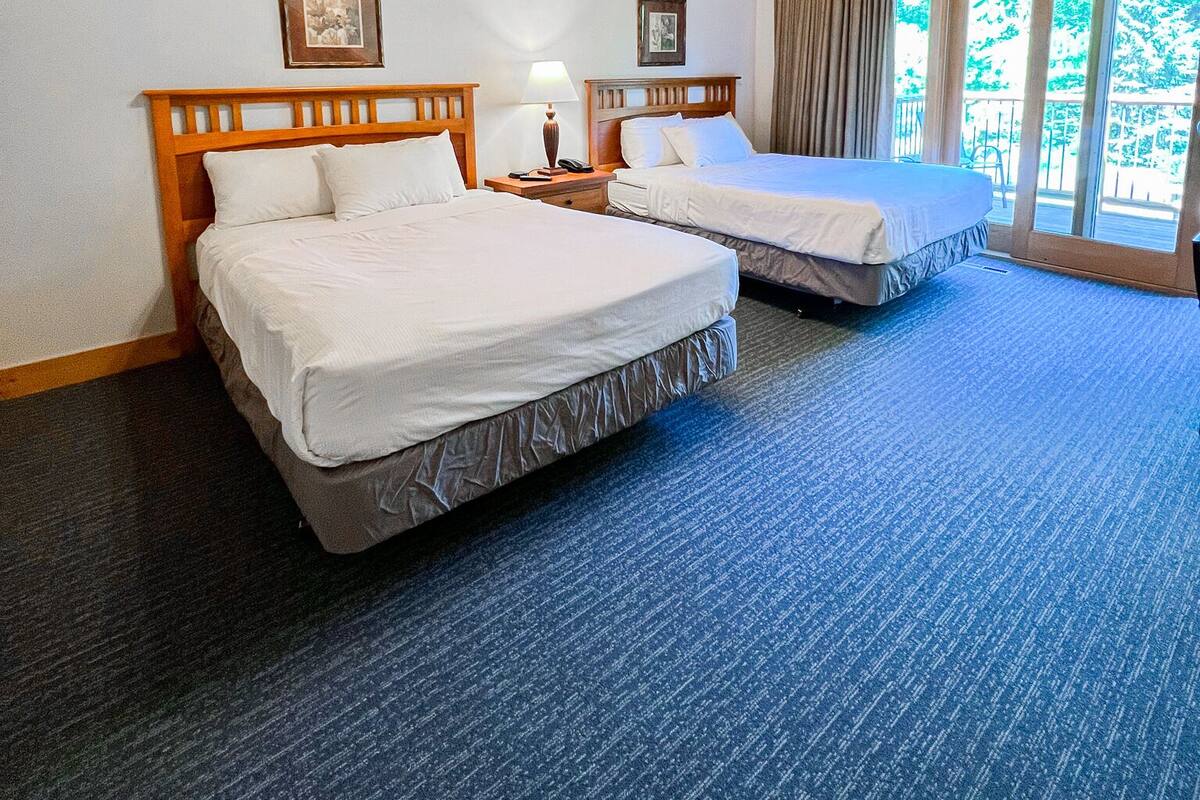 Habitación de hotel con dos camas, techo de madera y ventanas amplias.