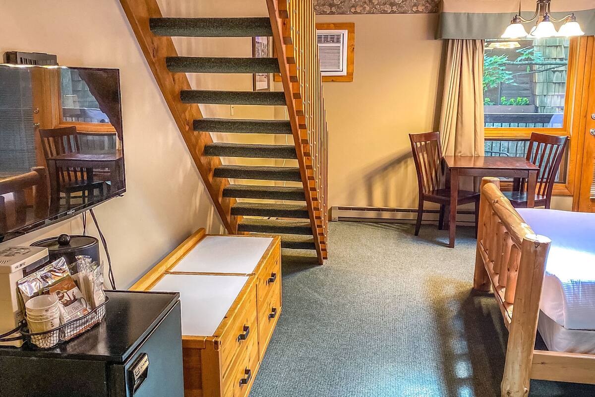 Una habitación con escalera de madera, cama, escritorio y televisor.