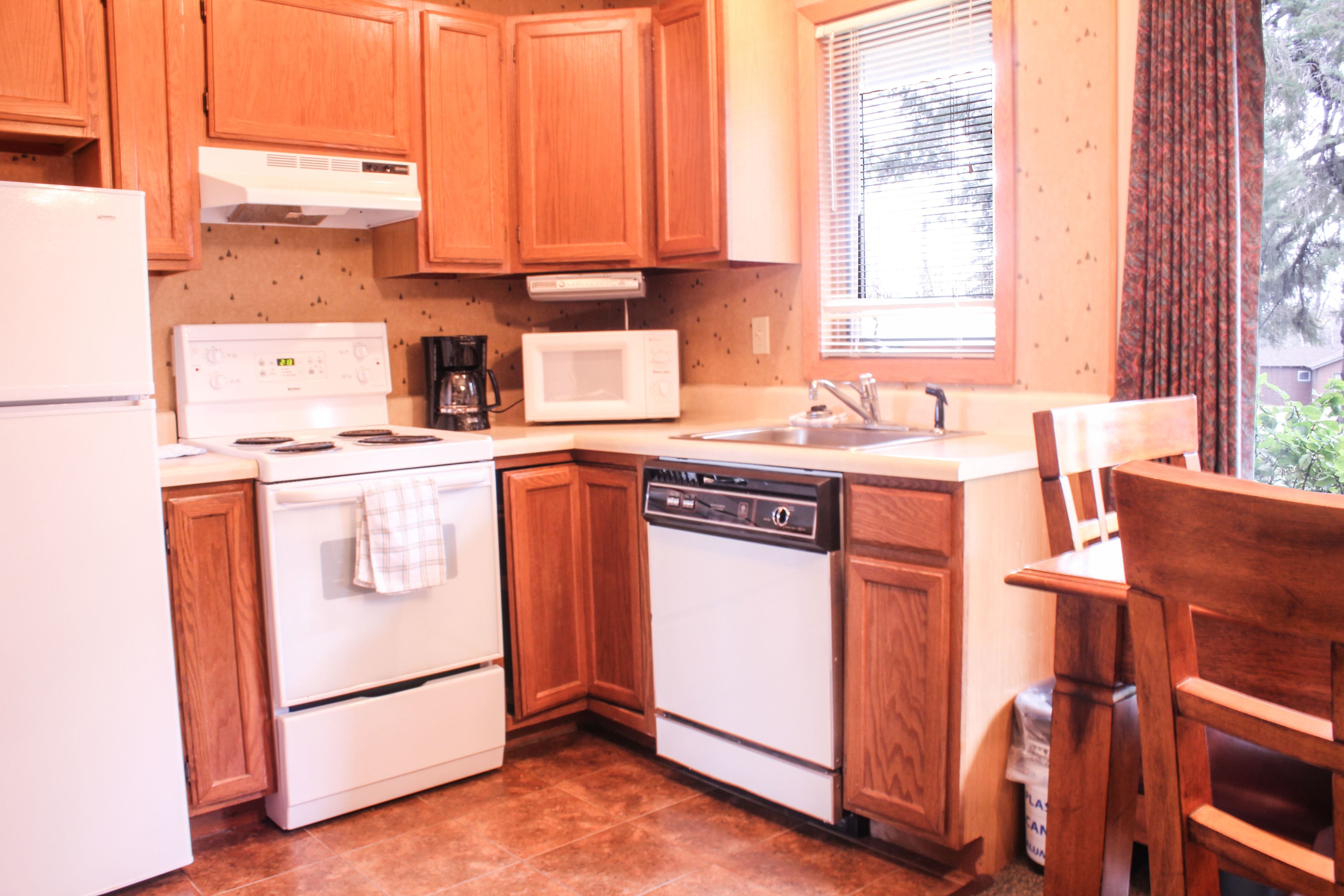 A kitchen with wooden cabinets, a white stove, a microwave, and a dishwasher.
