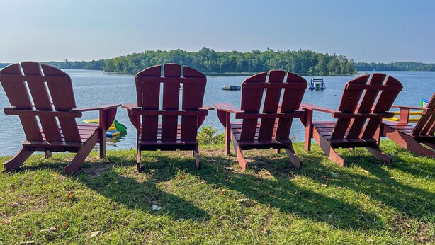 Four Adirondack chairs facing a lake with a forested island in the background.