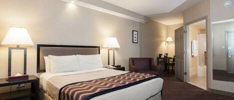 A hotel room with a large bed, two bedside lamps, a chair, a desk, and a door leading to a bathroom.