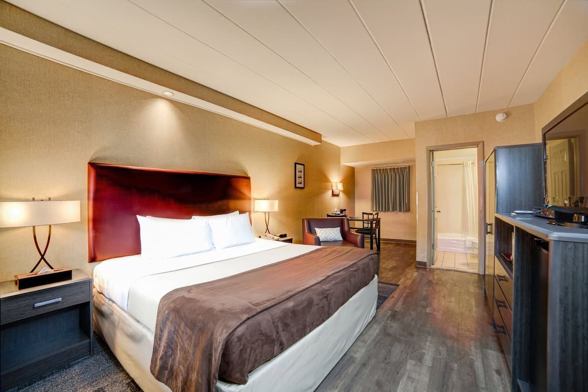 A hotel room with a large bed, bedside tables, a desk with a chair, a television, and a door leading to a bathroom.