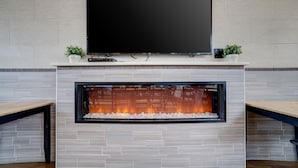 Una sala de estar moderna con un televisor de pantalla plana sobre una chimenea, flanqueada por dos macetas.