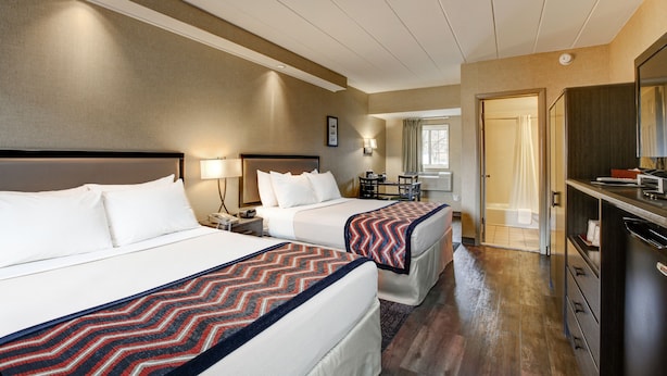 Habitación de hotel con dos camas, un escritorio, una silla, una cómoda y un baño visible a través de una puerta abierta.