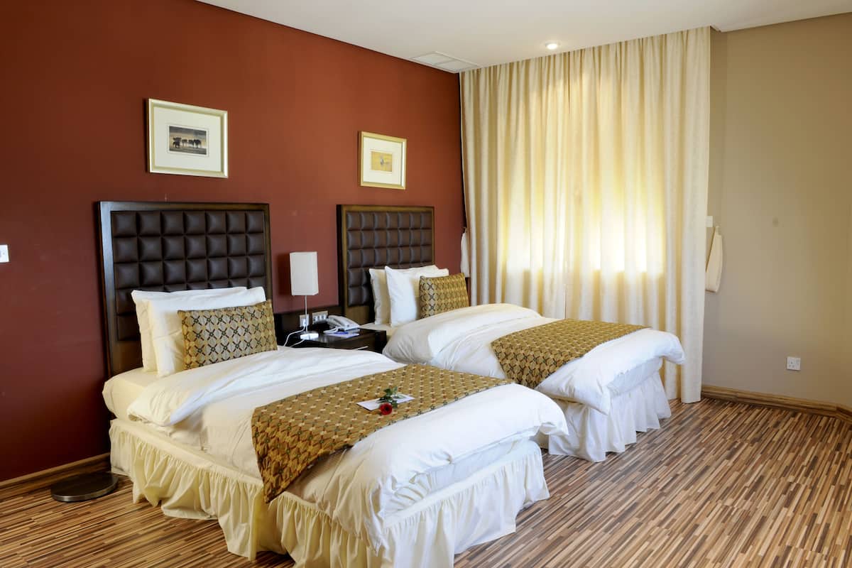 A hotel room with two beds, a large window with curtains, and a wooden floor.