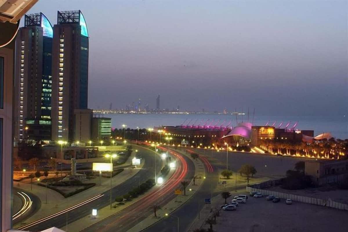 A balcony with a table and chairs, overlooking a cityscape with modern buildings and a road with moving vehicles.