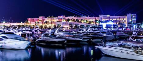 A marina at night with boats docked and a building with illuminated windows in the background.