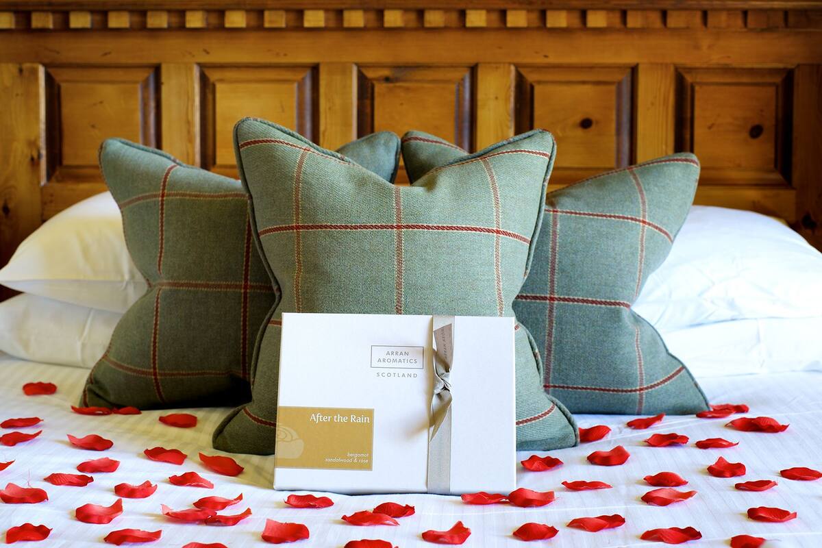 A bed with green plaid pillows, a box labeled "After the Rain" with red rose petals scattered on the bed.