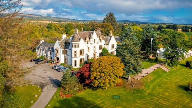 A large, white, multi-story house with a prominent turret and multiple chimneys, surrounded by lush greenery and a well-maintained lawn. - Kincraig Castle Hotel (Invergordon)