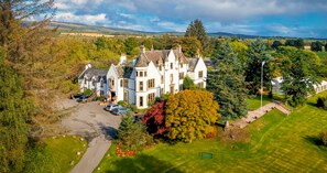 A large, white, multi-story house with a prominent turret and multiple chimneys, surrounded by lush greenery and a well-maintained lawn. - Kincraig Castle Hotel (Invergordon)