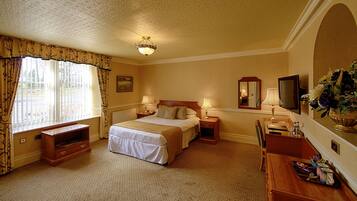 Quarto de hotel com uma cama grande, duas mesas de cabeceira, uma escrivaninha com cadeira, televisão e janela com cortinas.