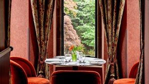 A dining area with a table set for two, curtains, and a view of greenery outside. - Kincraig Castle Hotel (Invergordon)