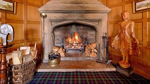 A room with a stone fireplace, a Buddha statue, and a plaid carpet. - Kincraig Castle Hotel (Invergordon)