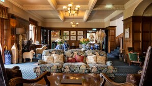A spacious lobby with a patterned sofa, leather armchairs, a chandelier, and a coffee table. - Kincraig Castle Hotel (Invergordon)