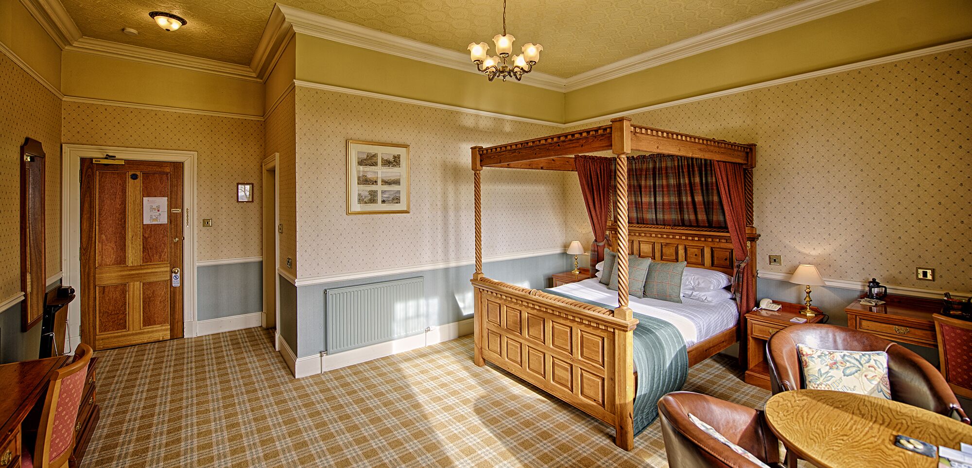 A four-poster canopy bed with a wooden frame, a bedside table with a lamp, a chair, and a small table with a telephone.