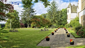 A well-maintained garden with a stone pathway leading to a building with a tower. - Kincraig Castle Hotel (Invergordon)
