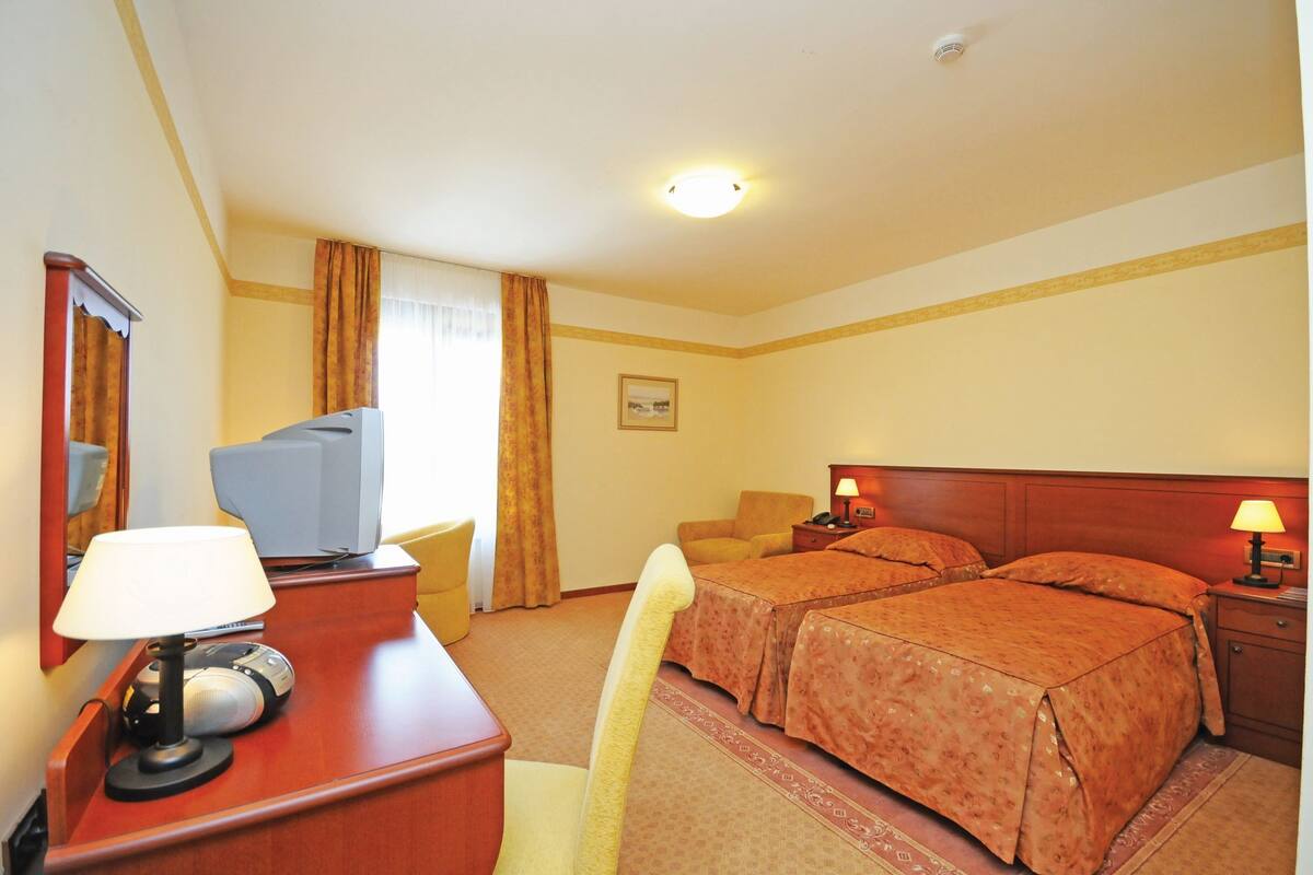 A hotel room with a bed, a desk with a lamp, a television, and a chair.