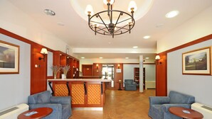 A lobby with a reception desk, two armchairs, a small table, and a chandelier.