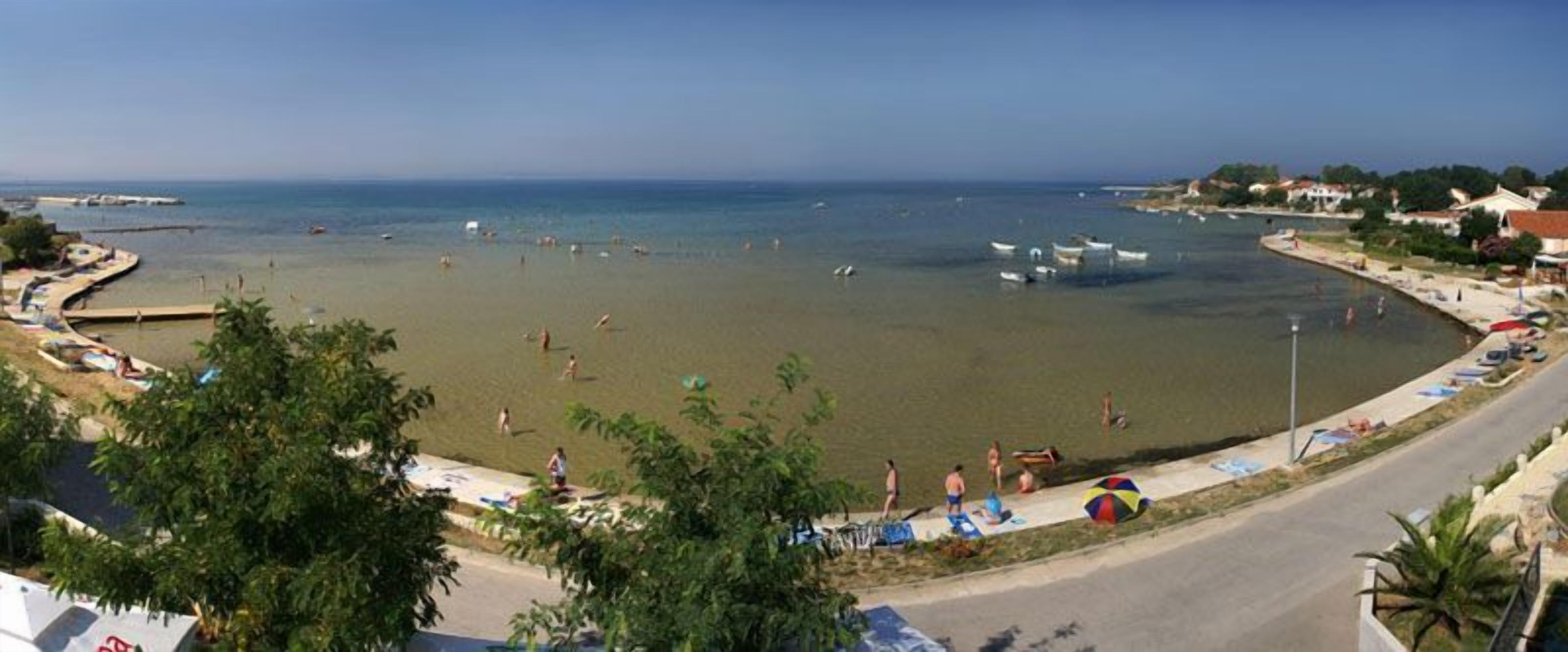 A beach with clear water, people swimming, and boats.