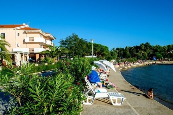 Un hotel frente al mar con zona de piscina, sillas de descanso y sombrillas.